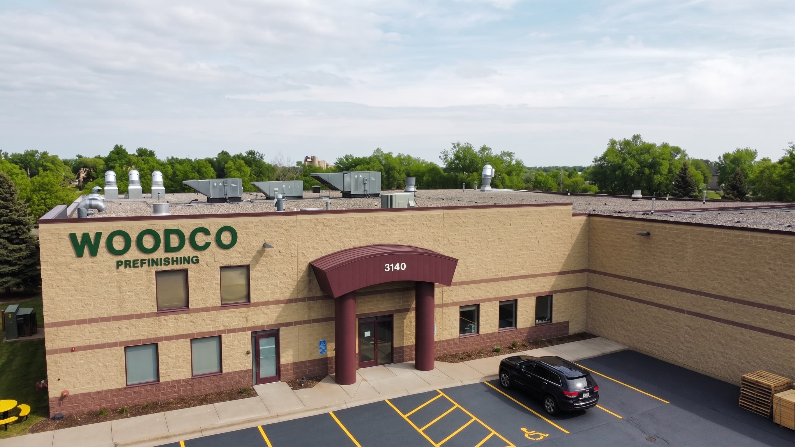 Aerial drone view of the Woodco Prefinishing facility exterior in Blaine, Minnesota, showing the branded WOODCO PREFINISHING signage at 3140 103rd Lane NE