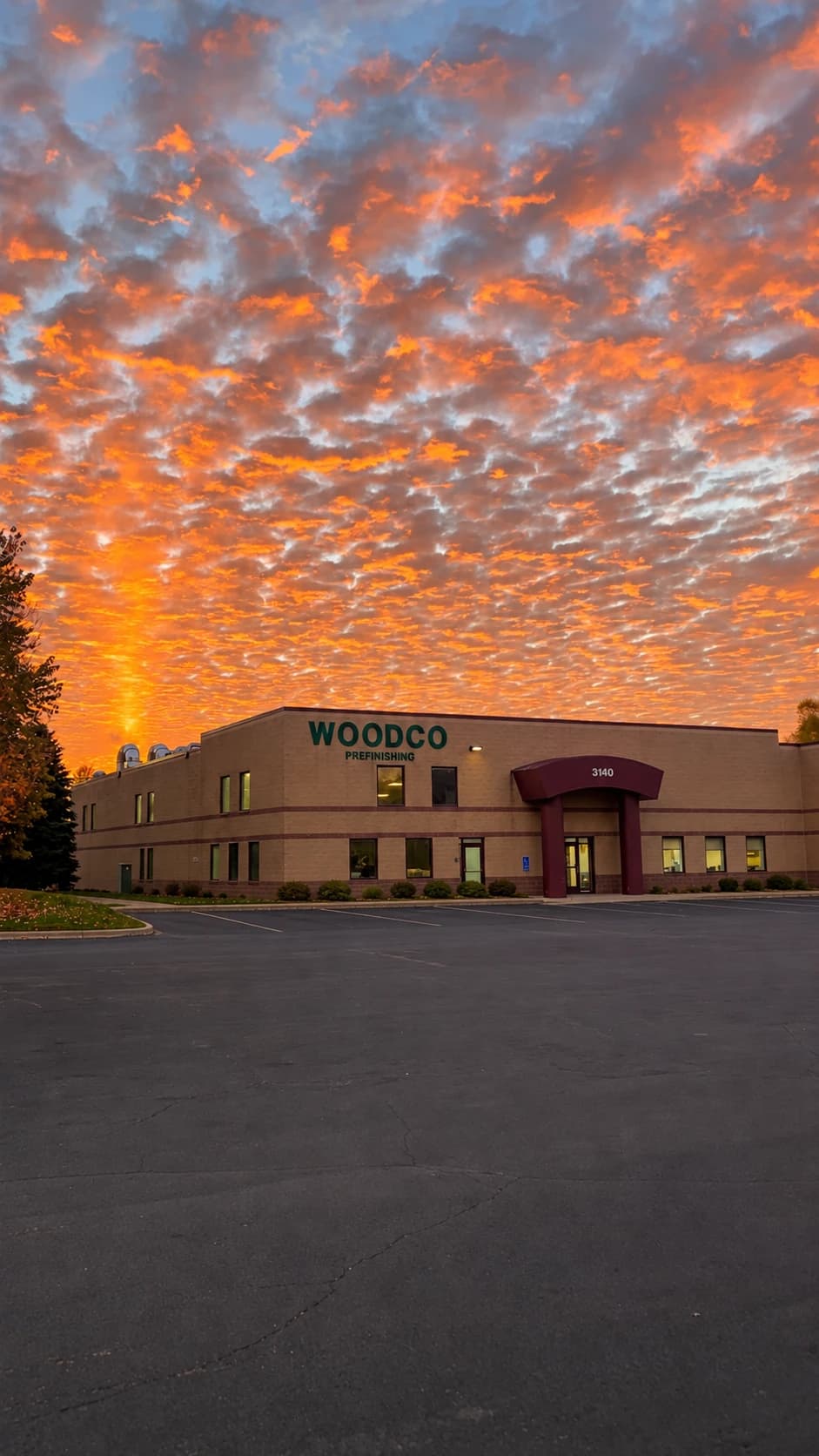 Woodco Prefinishing facility at 3140 103rd Lane NE in Blaine, Minnesota, with its green WOODCO PREFINISHING signage under an orange sunset sky