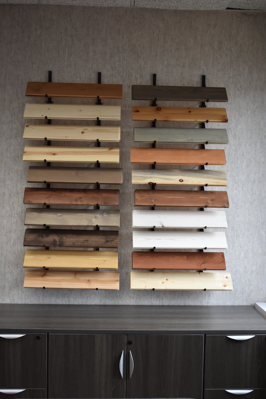 Wall-mounted color sample display showing the full Woodco stain library on vertical wood slats