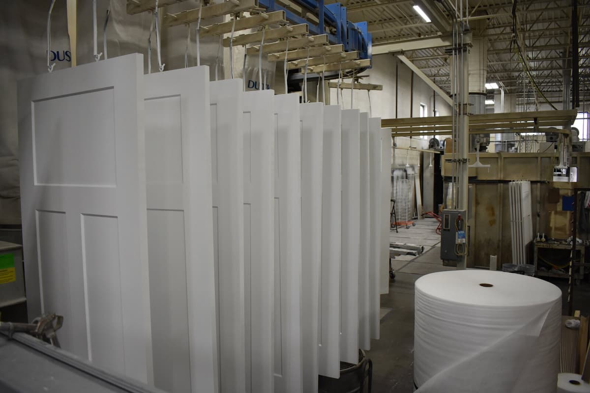 Finished white interior doors hanging on the overhead conveyor finishing line at Woodco