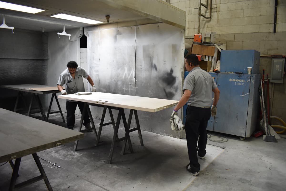 Two finishers spraying a large panel on sawhorses inside a Woodco spray booth